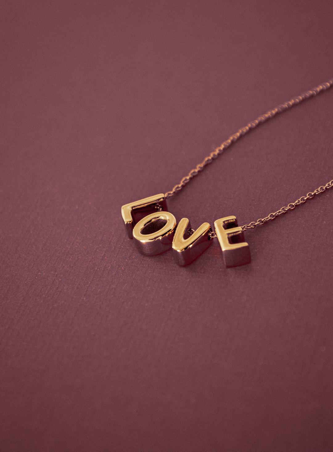 "Love Letter" Halskette in Gold auf weinrotem Untergrund