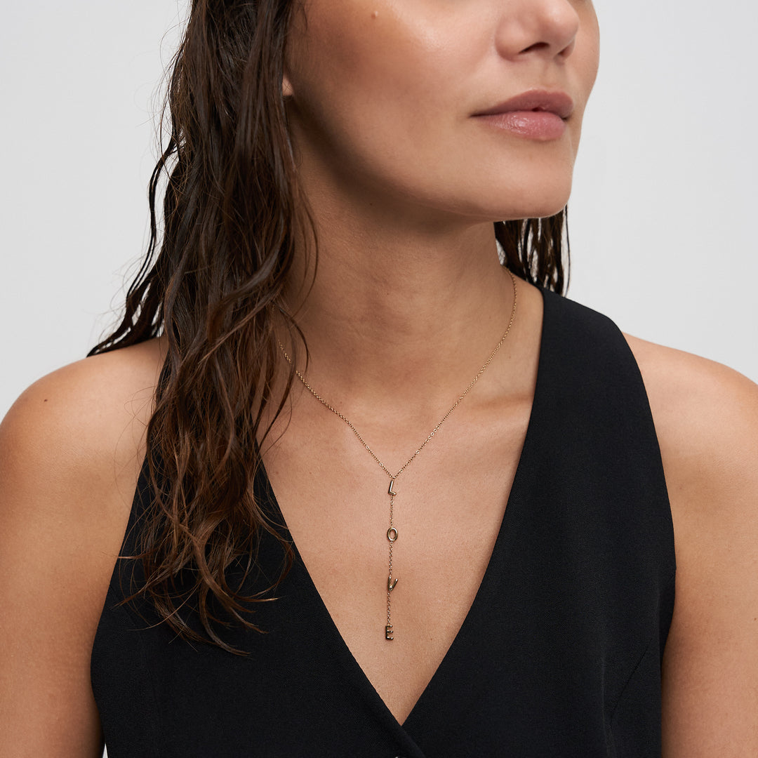 Model trägt die goldene ECHTZEIT Love Letters Y-Halskette zum schwarzen Top – ein moderner Schmuck-Look mit LOVE-Statement.